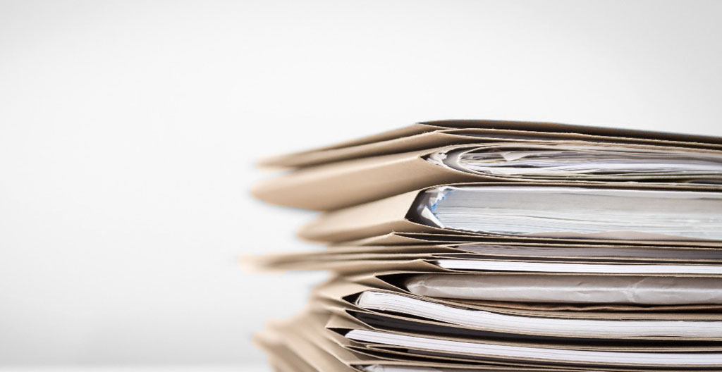 Gros plan sur les mains d'une personne remplissant un formulaire administratif avec un stylo bleu sur une table en bois clair, une tasse de café blanche floue en arrière-plan